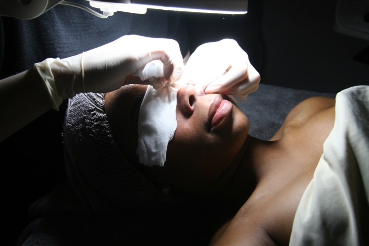 A woman under a light receiving a facial