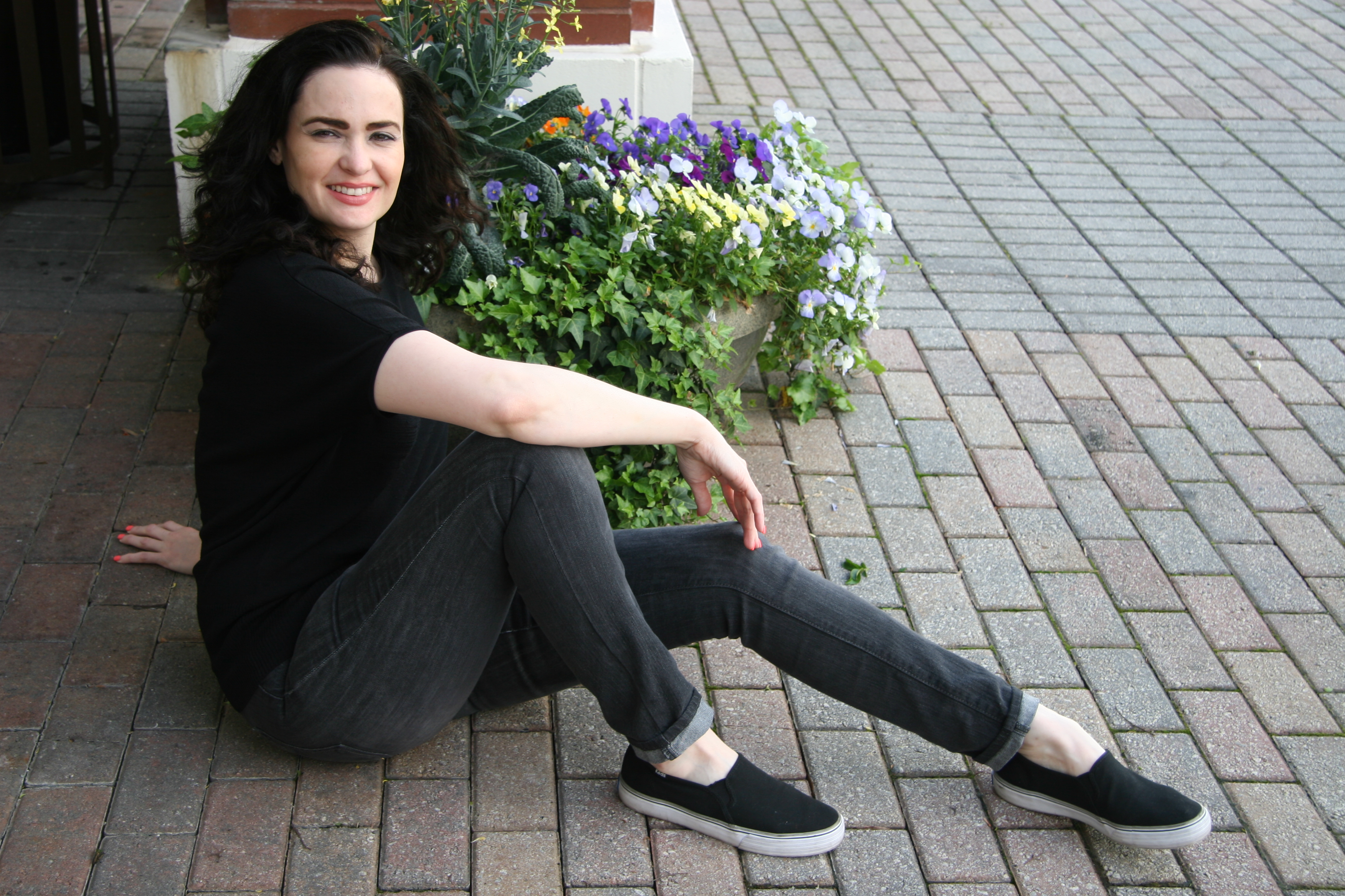 A woman in a black shirt and jeans sitting next to flowers