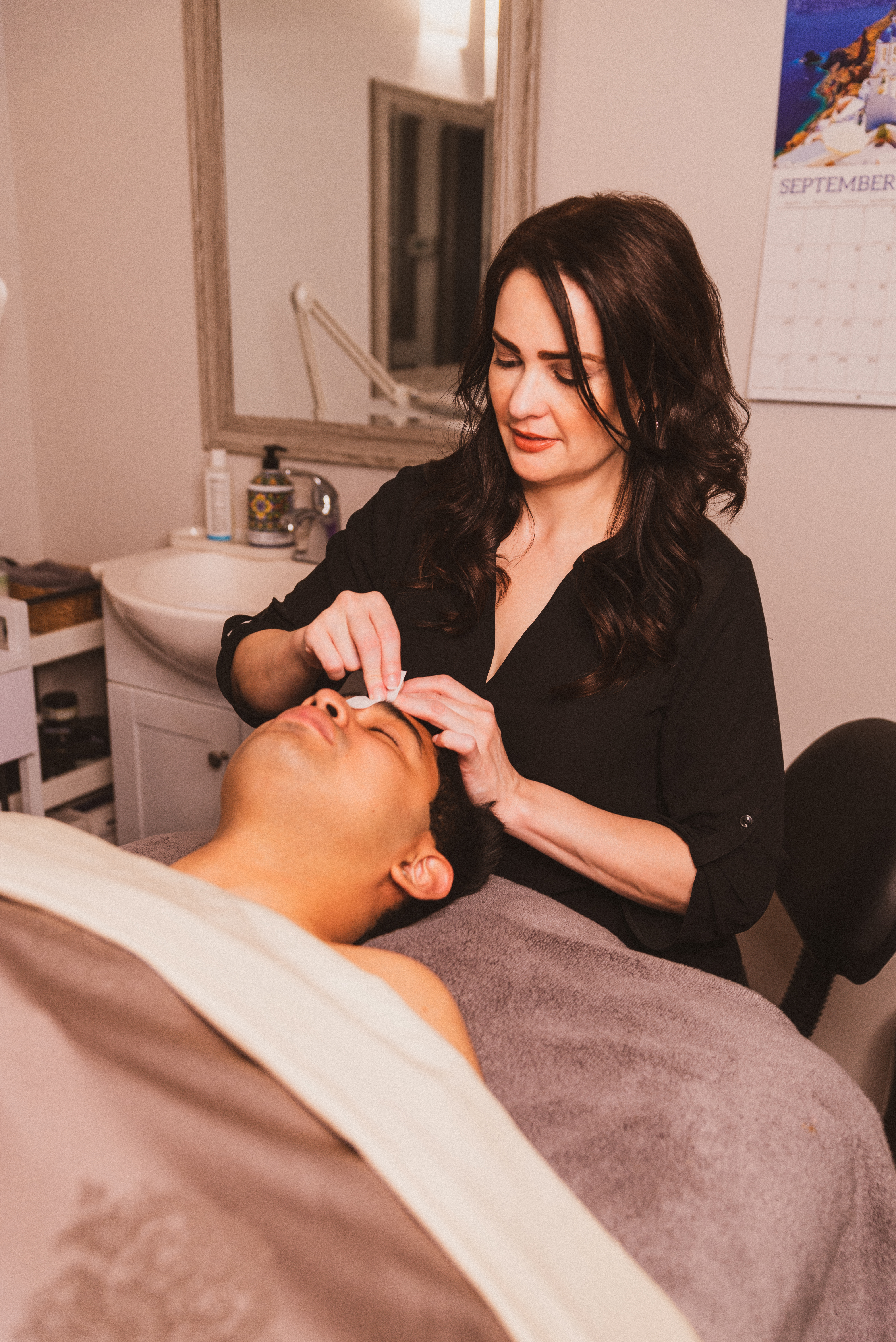 A woman in a black shirt putting a white cloth over a man's eyebrow during a treatment