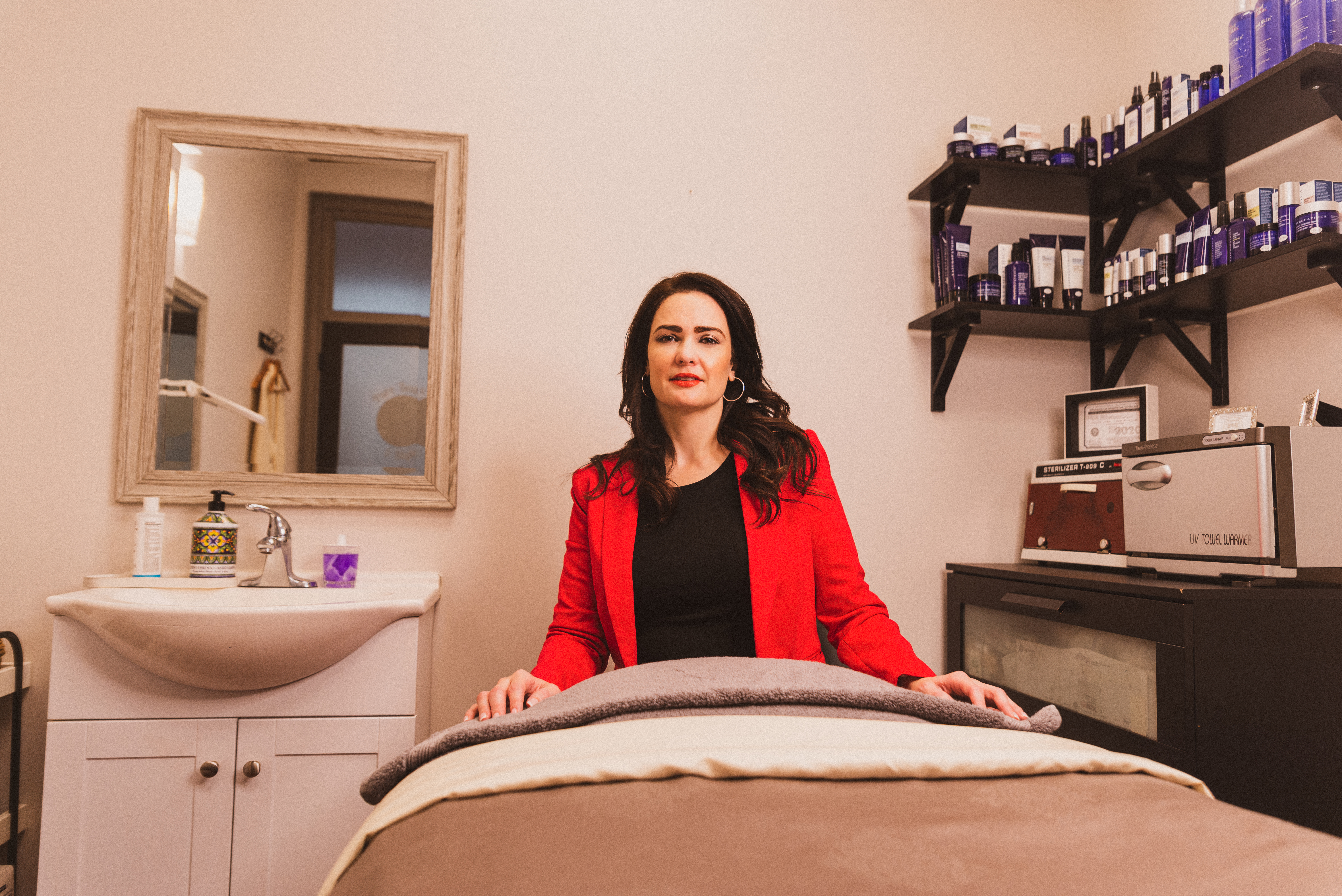 A woman in a red blazer sitting behind a table where she performs treatments