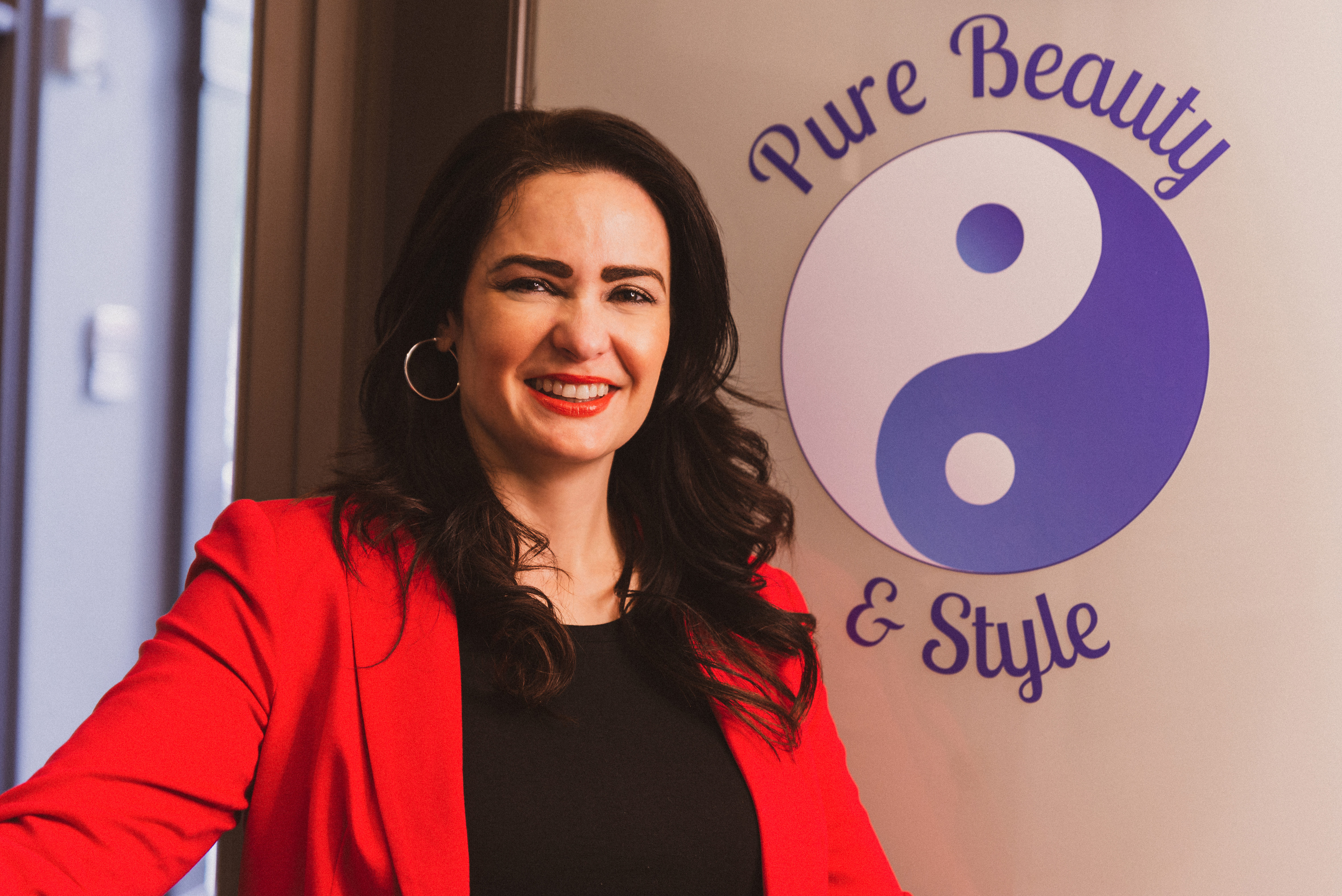 A woman in a red blazer next to her logo, a yin-yang symbol with the words Pure Beauty and Style around the outer edge