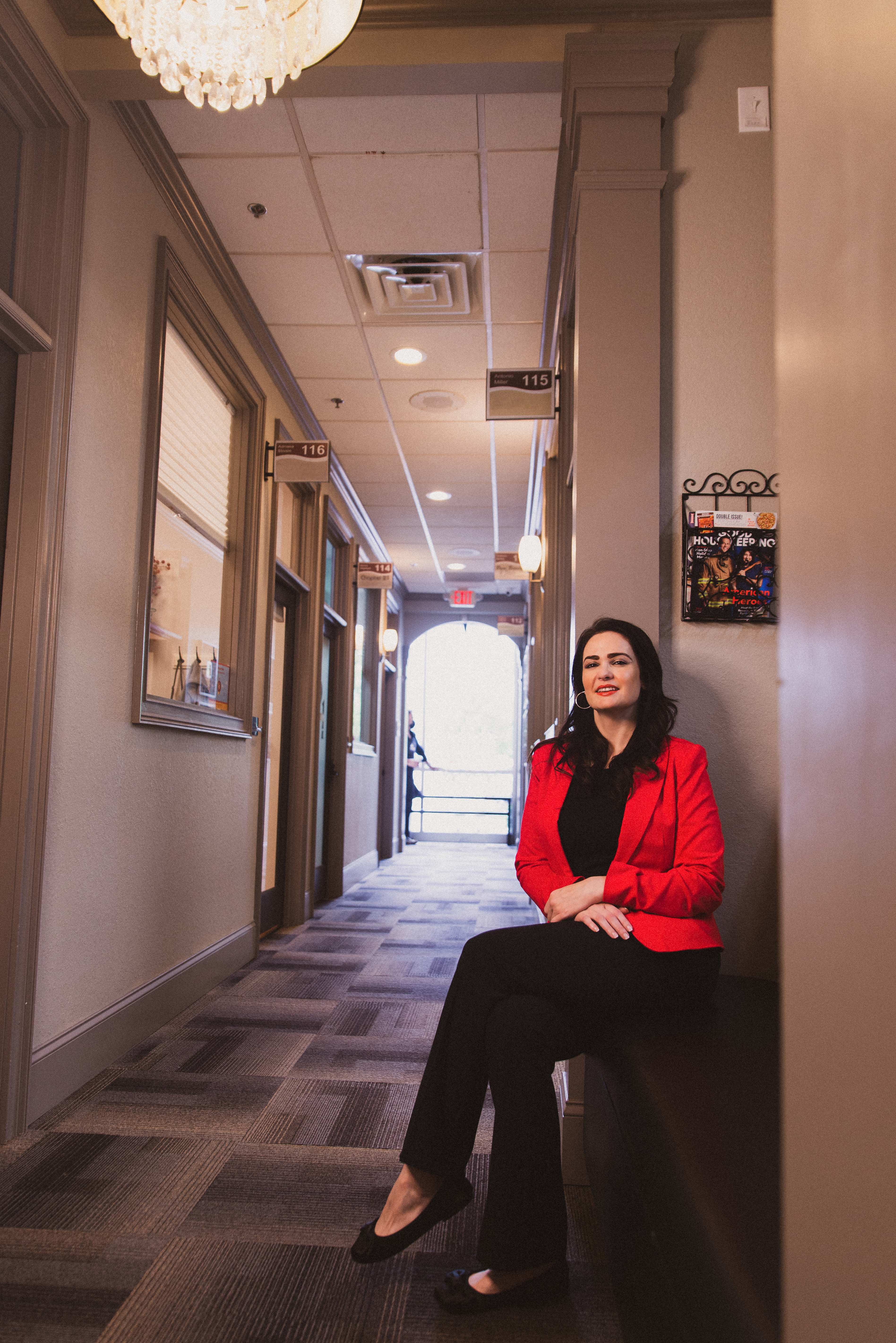 A woman in a red blazer and black pants in the hallway outside of her office