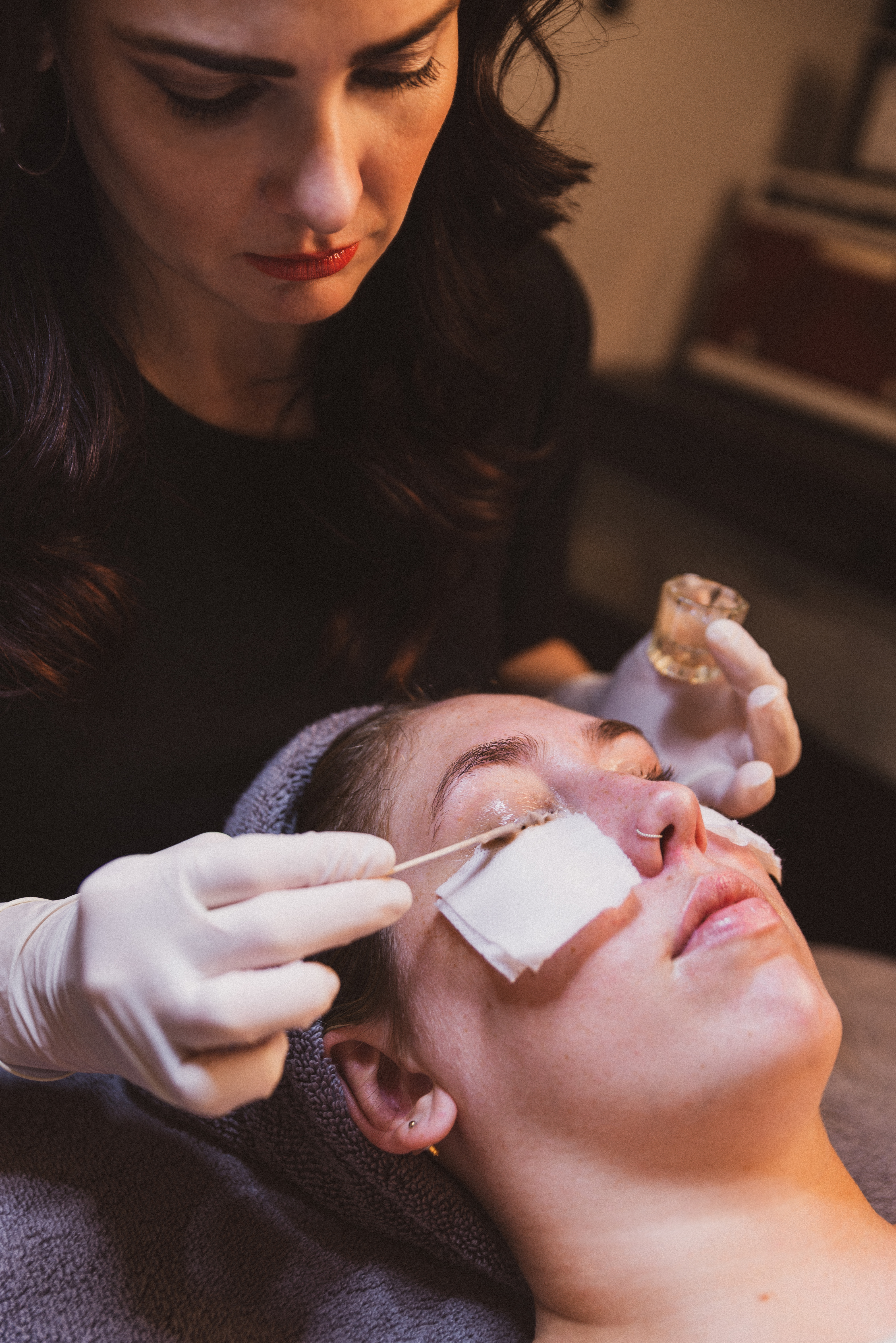 A woman wearing gloves putting gel on a client's eyelids